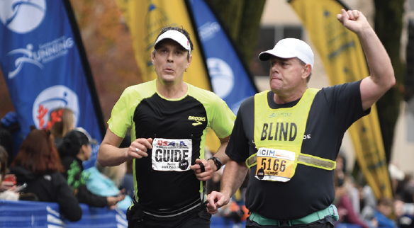 Richard Hunter wearing blind vest with arm triumphantly in air running with a guide.