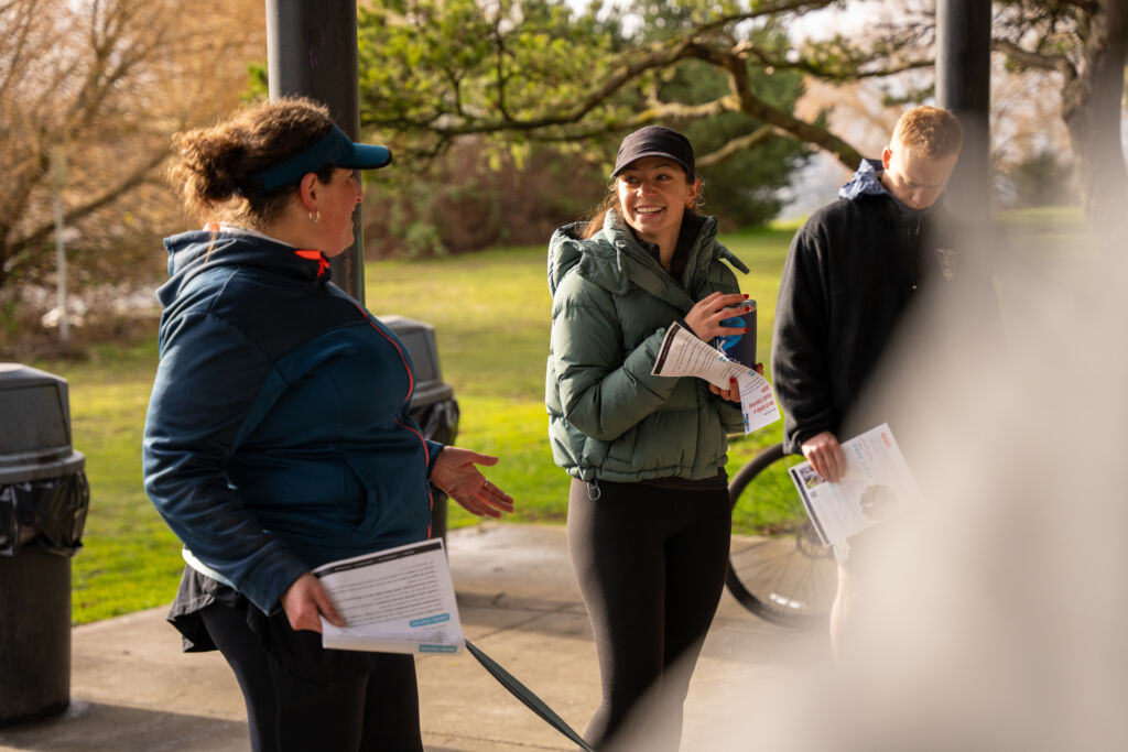 A group of people conversing outside in jackets, holding packets at a training