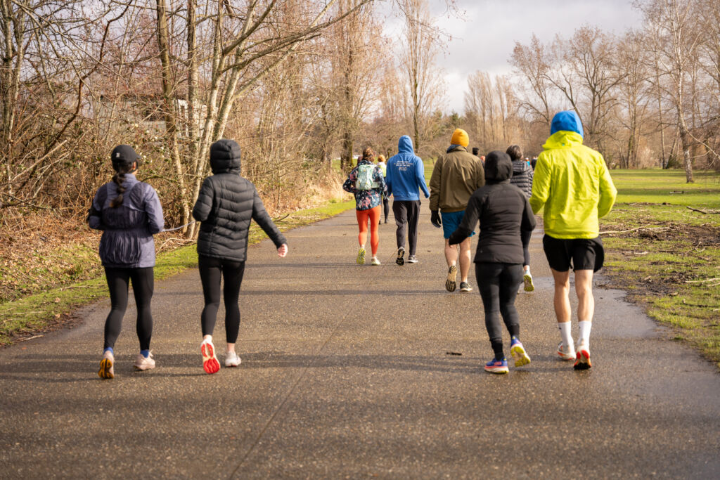 Many people in athletic attire running down a paved path in a park