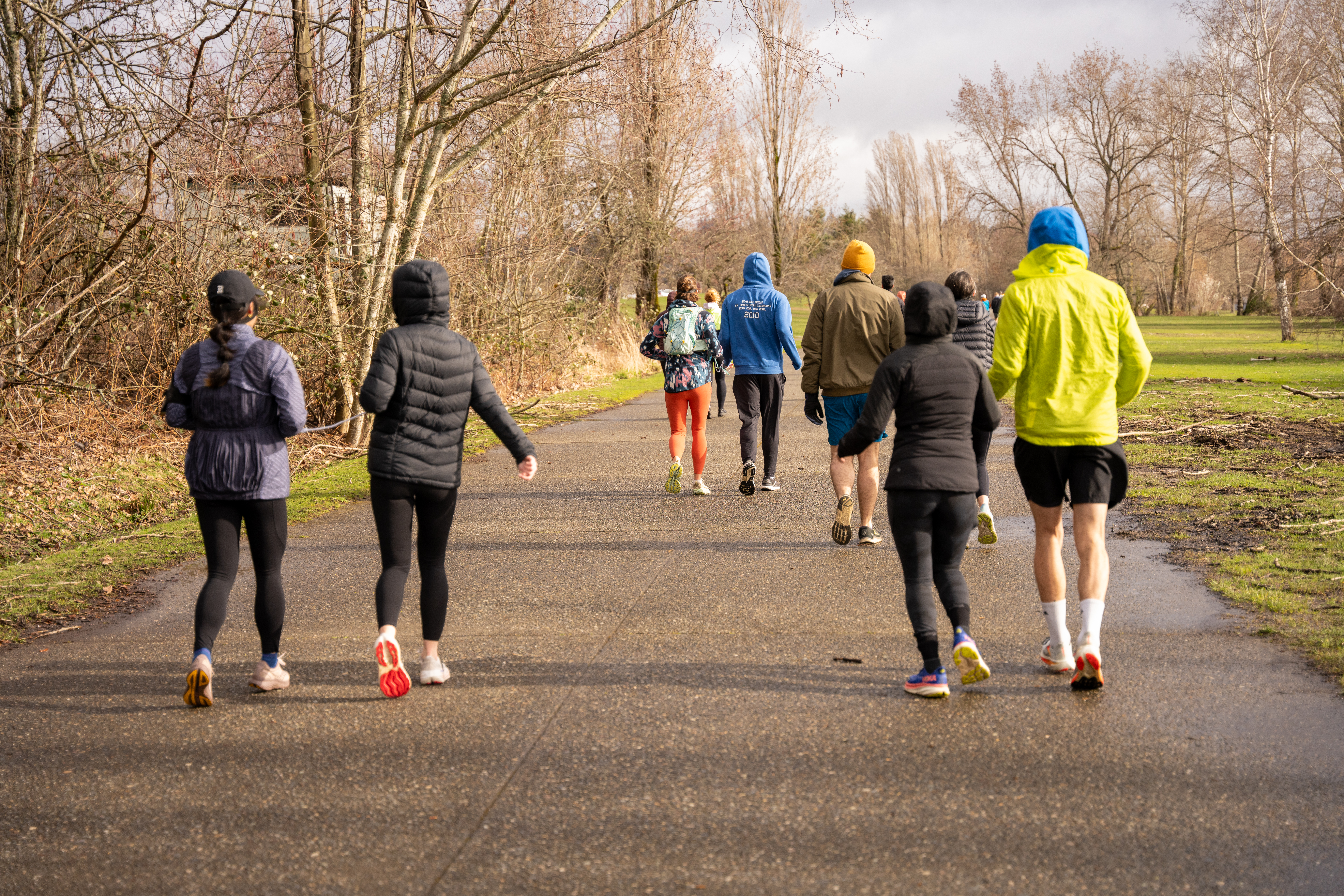 Many people wearing athletic attire running down a paved path in an outdoor park